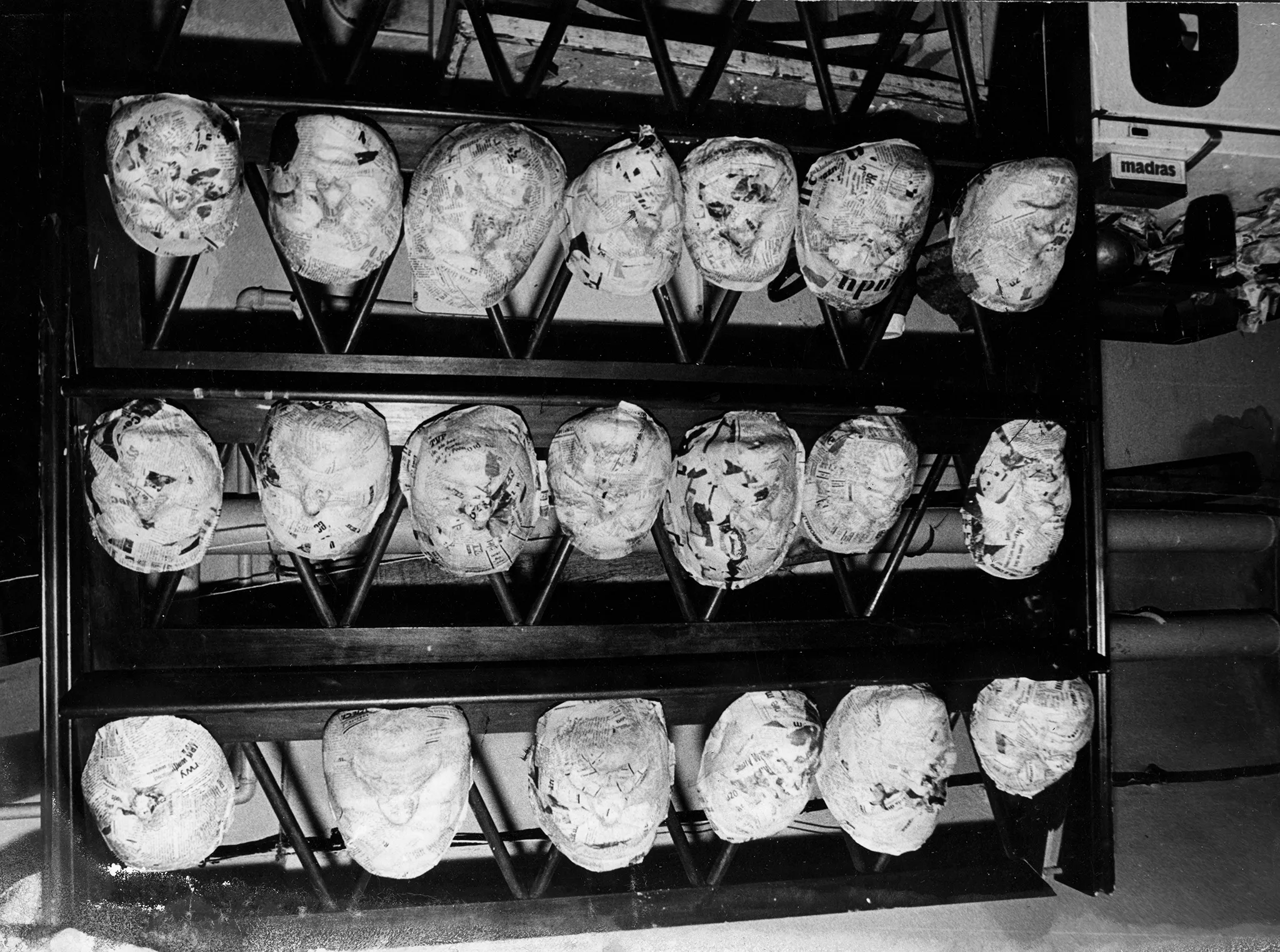 Trzy półki, na których ustawione są okrągłe przedmioty. Wyglądają jak maski teatralne.