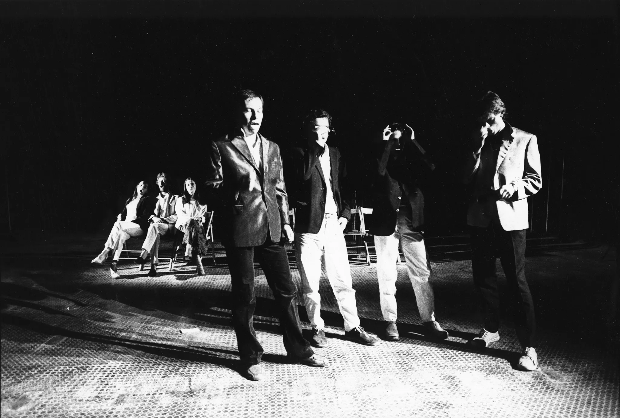 Przestrzeń miejska. Grupa aktorów i aktorek rozwija na ulicy między budynkami wielką biała płachtę. W tle widać samochody i przechodniów.