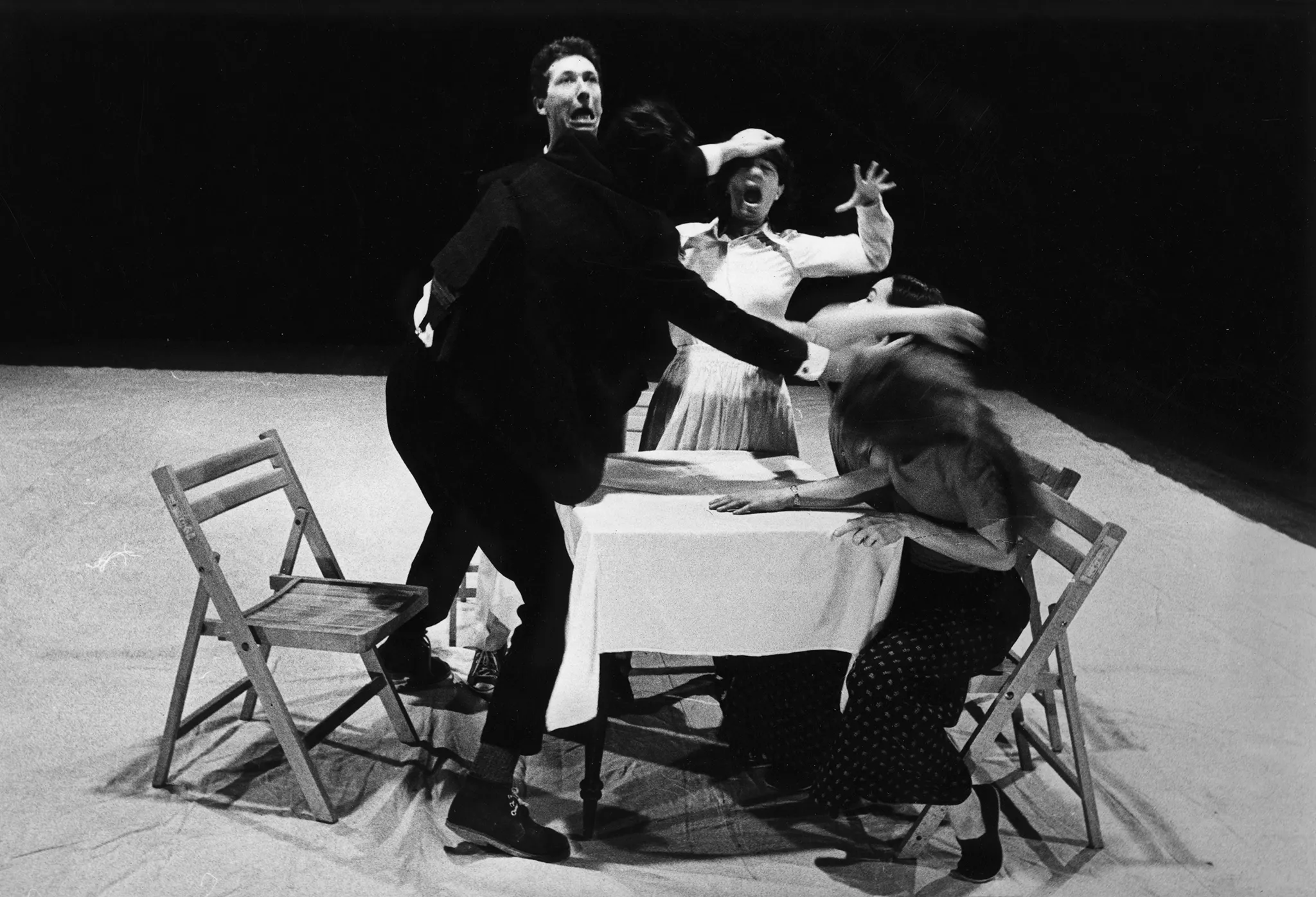 Grupa aktorów i aktorek na krzesłach przy stoliku. Wyglądają, jakby się awanturowali.