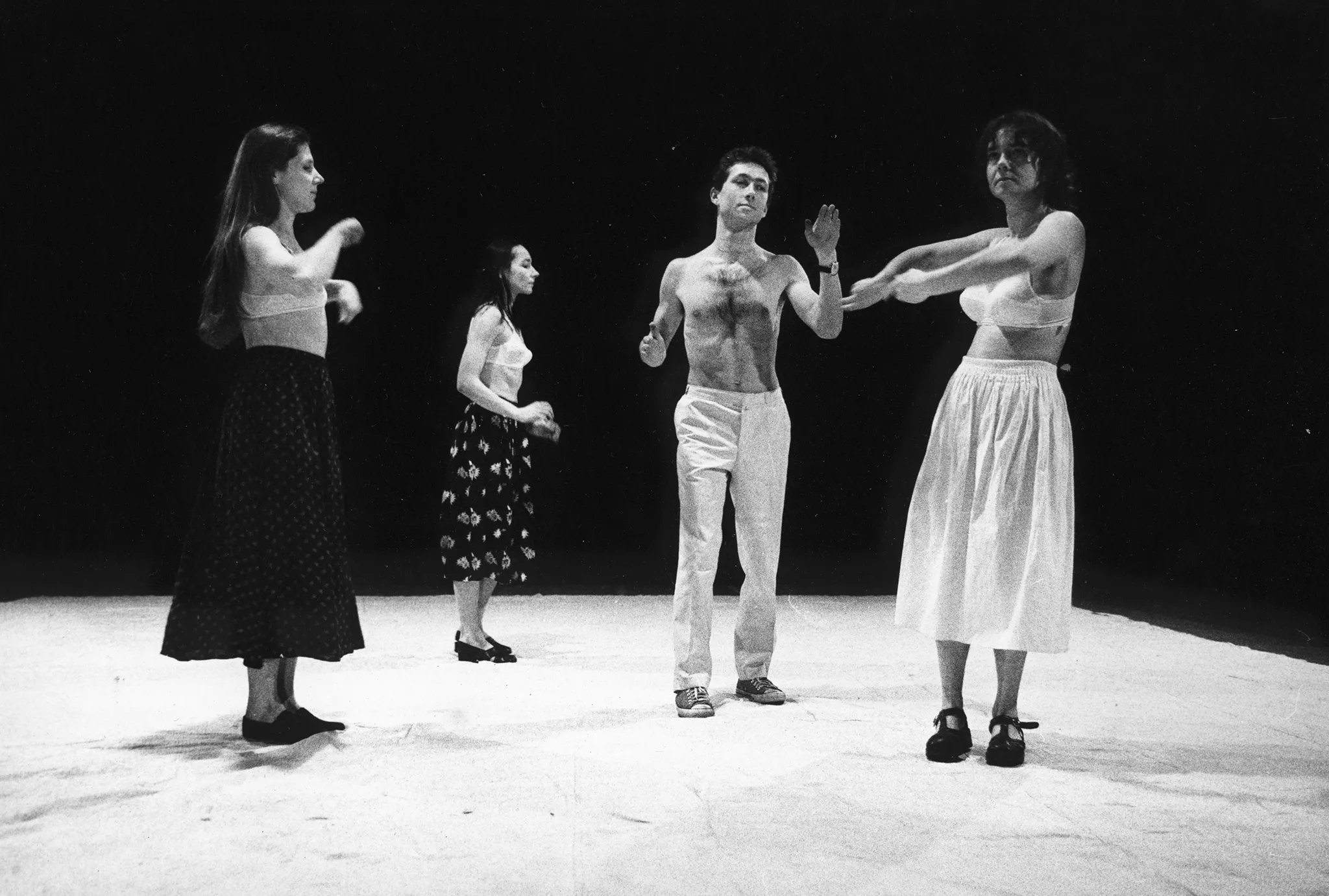 Na scenie stoją trzy aktorki i jeden aktor. Aktorki ubrane są w spódnice i staniki. Aktor jest ubrany w jasne spodnie i ma nagi tors. Wszyscy gestykulują dłońmi.