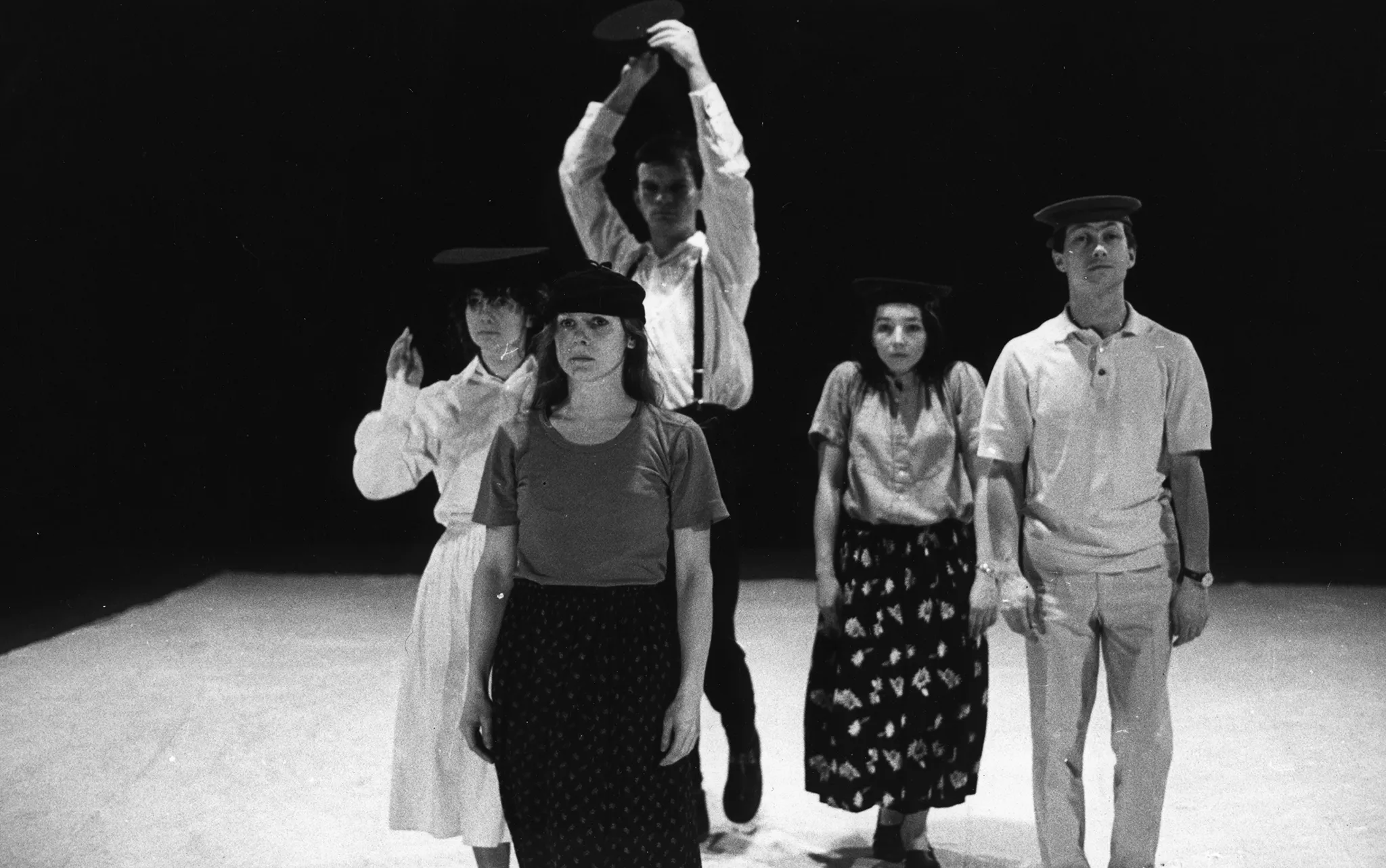 Pięcioosoba grupa aktorów i aktorek stoi zwrócona twarzą w stronę widza. Wyglądają na poważnych. Każdy ma czarne nakrycie głowy.