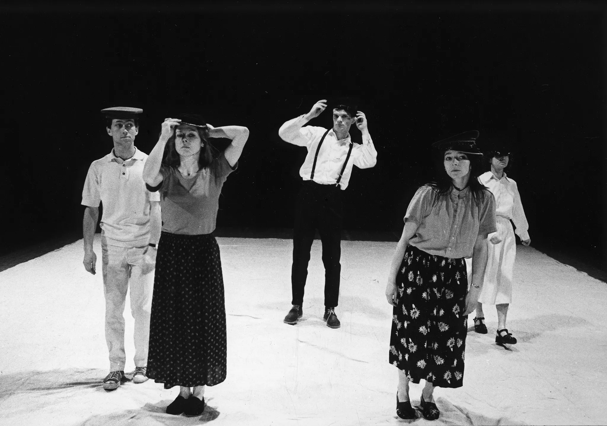 Pięcioosoba grupa aktorów i aktorek stoi na białej płachcie zwrócona twarzą w stronę widza. Każdy ma czarne nakrycie głowy.
