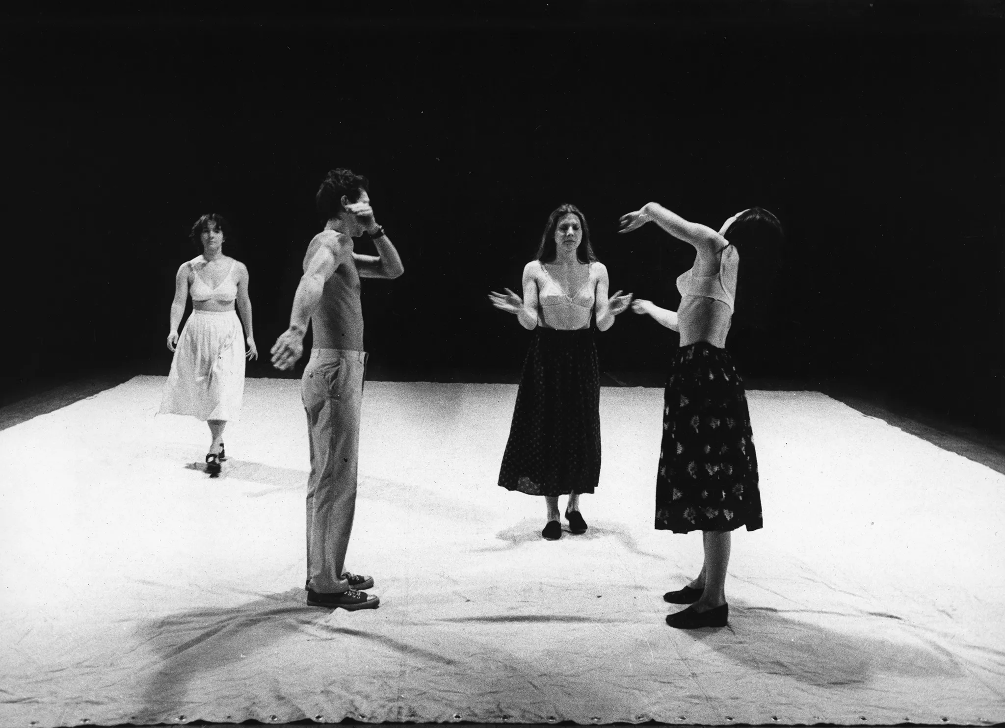 Na białej plachcie stoją trzy aktorki i jeden aktor. Aktorki ubrane są w spódnice i staniki. Aktor jest ubrany w jasne spodnie i ma nagi tors. Dwie aktorki zwrócone są twarzą w stronę widza. Jedna aktorka i aktor są zwróceni twarzą w swoją stronę, profilem do widza.