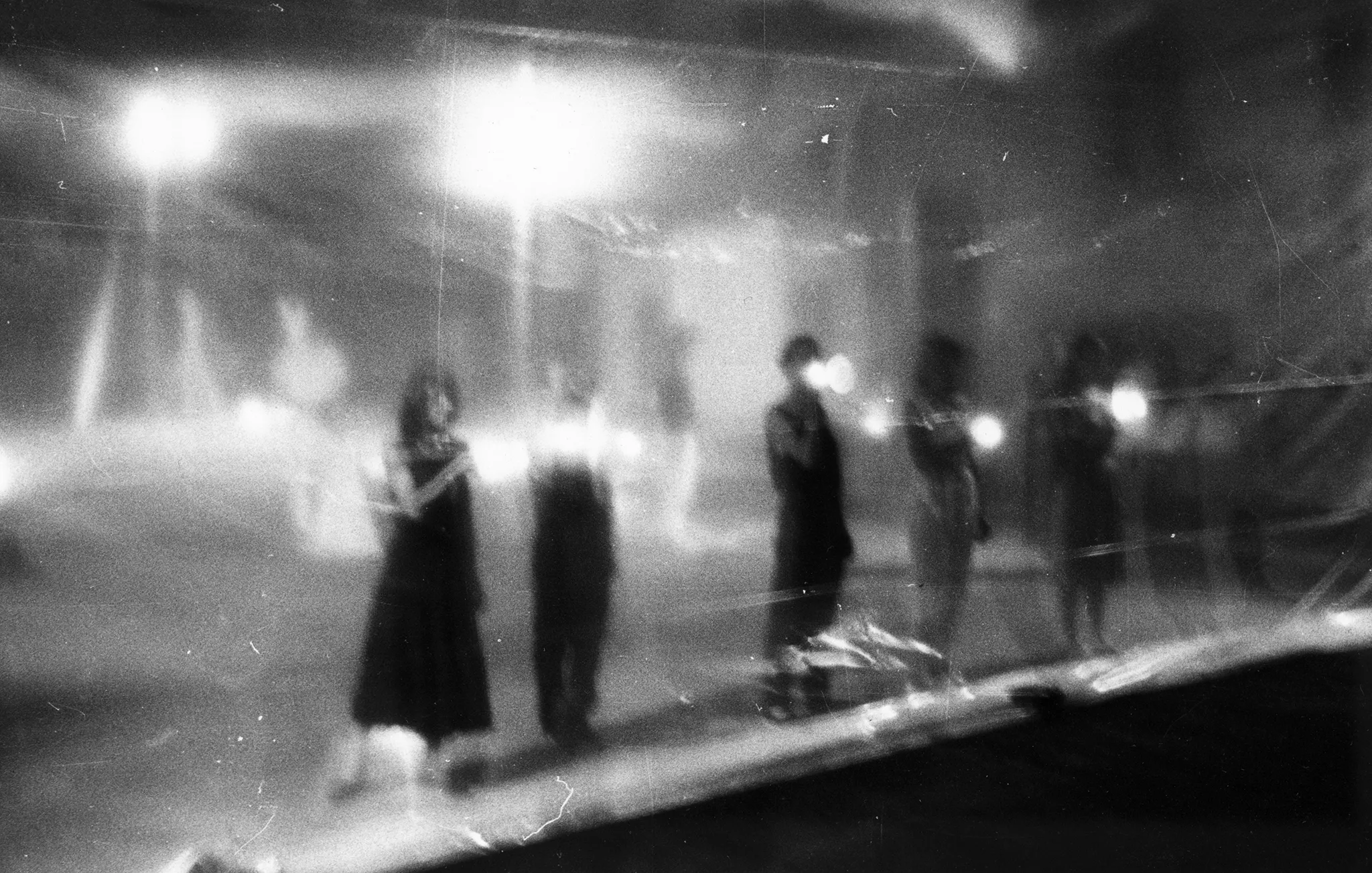 Niewyraźne zdjęcie. Grupa aktorów i aktorek stoi w szeregu za przeźroczystą płachtą. W rękach trzymają latarki.