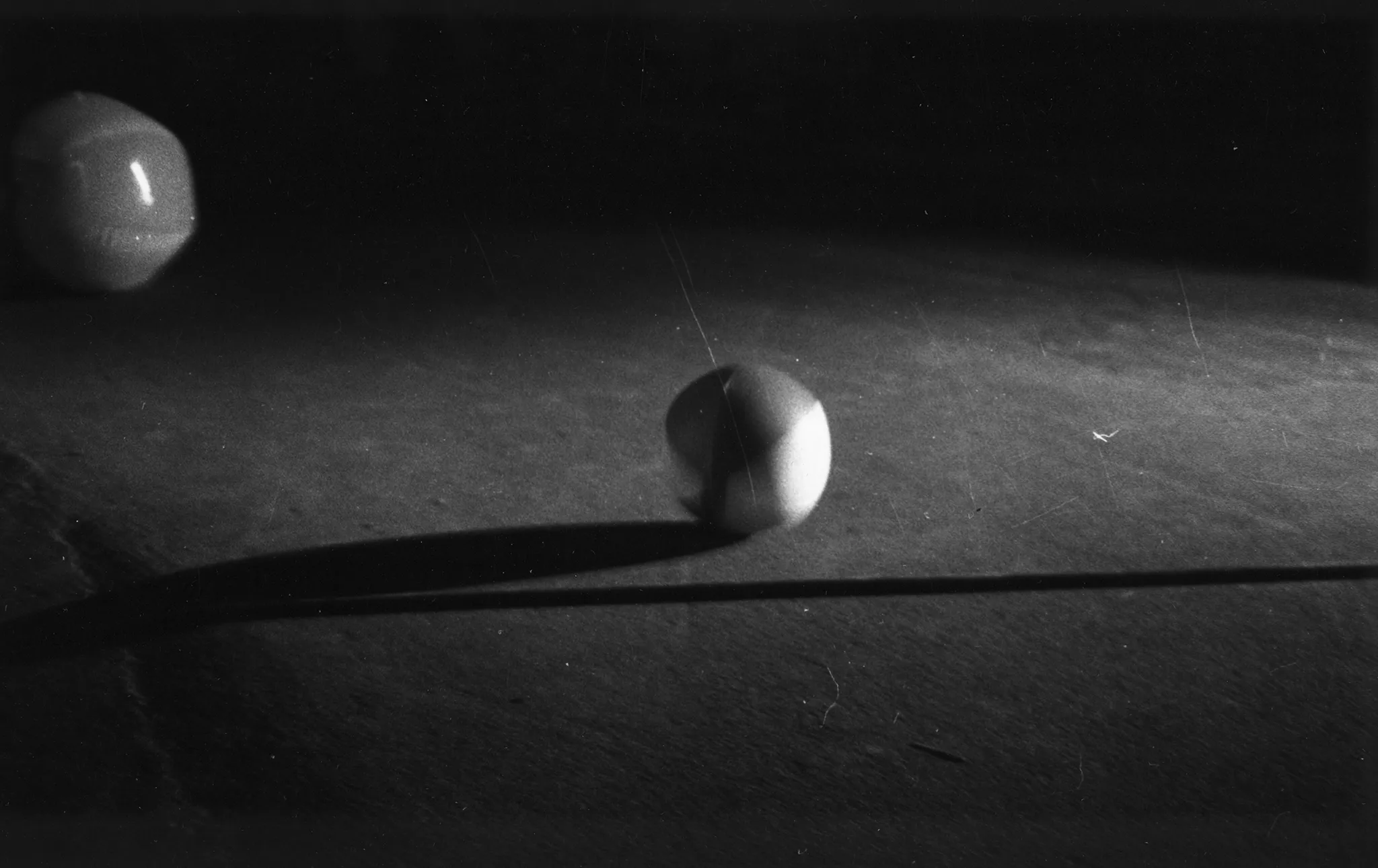 W centrum leży różnokolorowa mała piłka rzucająca cień na podłogę. Za nią, po lewej stronie leży podobna piłka większych rozmiarów.